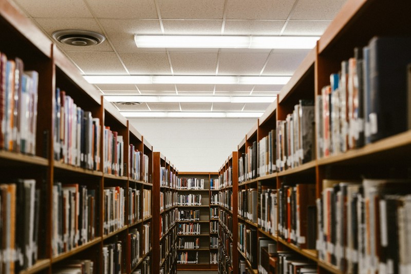 Corredor de biblioteca com estantes de livros em instituição de ensino.